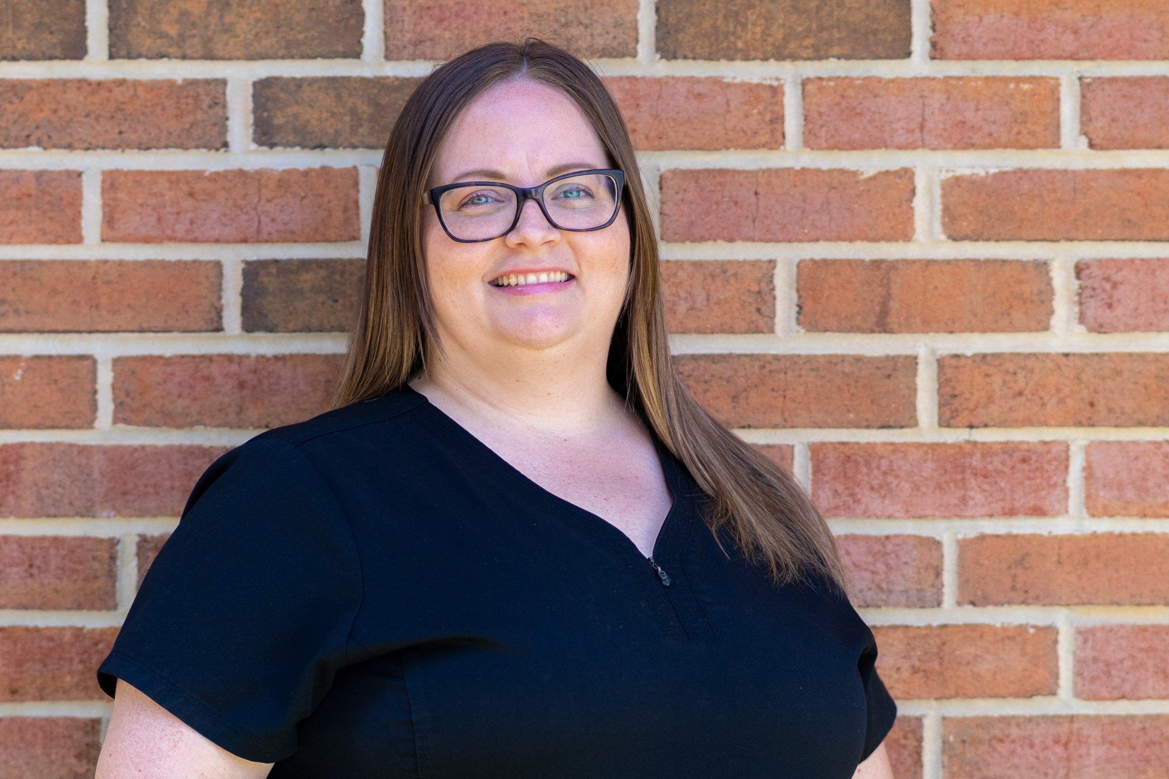 a woman wearing glasses standing in front of a brick wall